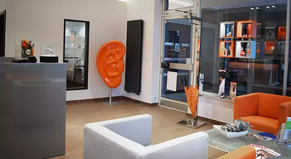 Modernes Hörakustik-Fachgeschäft mit orangenem Ohr-Dekor und gemütlicher Sitzecke.